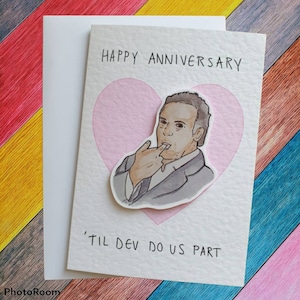 Könnte beinhalten: Eine weiße Karte mit einem rosa Herz und einer Cartoon-Illustration eines Mannes im Anzug. Der Text auf der Karte lautet "Happy Anniversary 'Til Dev Do Us Part".
