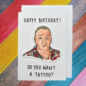 May include: A white card with the text "Happy Birthday!" and a cartoon illustration of a person with a serious expression. The text "Do you want a tattoo?" is below the illustration.
