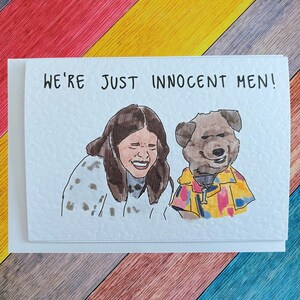 May include: A greeting card featuring a hand-drawn illustration of a woman and a dog. The woman is laughing and the dog is smiling. The text on the card reads "We're just innocent men!"