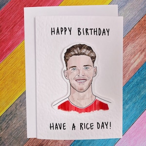 May include: A white card with the text "Happy Birthday" and a cartoon drawing of a man with brown hair. The text "Have a Rice Day!" is at the bottom of the card.