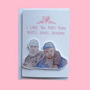 May include: A greeting card with a watercolor illustration of two men wearing hats. The card says "I love you more than Beats loves Grindah!" with pink hearts above the text.