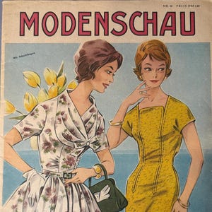 Könnte beinhalten: Vintage Zeitschriften-Cover "Modenschau" mit Illustrationen von zwei Frauen in Kleidern. Eine trägt ein Blumenkleid, die andere ein gelbes Kleid. Das Cover hat einen hellblauen Hintergrund und Text in Rosa und Weiß.