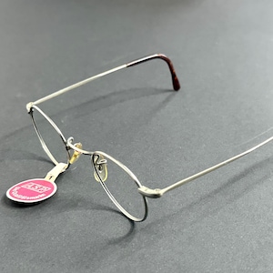 Peut inclure: Lunettes argentées avec des verres ovales et des branches marron. Les lunettes ont un design délicat en fil de fer et une petite étiquette attachée à la monture. L'étiquette est rose et blanche avec du texte.