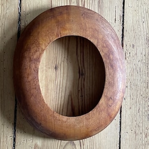 Könnte beinhalten: Ein kreisförmiges Holzobjekt mit einer großen zentralen Öffnung. Das Holz hat einen warmen, braunen Farbton mit sichtbarer Maserung und leichten Farbvariationen. Das Objekt scheint ein dekorativer Rahmen oder Teil eines größeren Stücks zu sein.