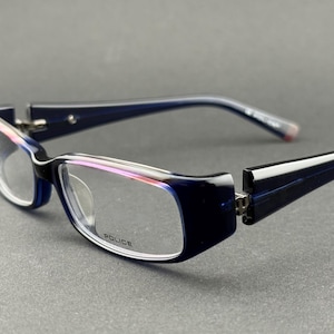Könnte beinhalten: Rechteckige Brille in Marineblau mit klaren Gläsern. Die Fassungen haben einen weißen und rosa Akzent. Auf dem Glas steht das Wort "POLICE". Ein stilvolles Accessoire.