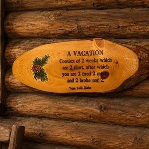 May include: An oval-shaped natural wood slice sign with bark edges featuring a painted pinecone and green needles. The text reads: A VACATION Consists of 2 weeks which are 2 short, after which you are 2 tired 2 return and 2 broke not 2. Twin Falls, Idaho.