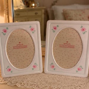 May include: Two identical white rectangular picture frames with rounded corners and an oval center opening. Each frame features four small hand-painted pink rose motifs with green leaves in the corners. The insert paper displays the Hallmark logo.