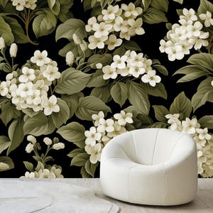 May include: A white, curved armchair sits in front of a black floral wallpaper. The wallpaper features white flowers and green leaves. The chair is a solid, off-white color and has a rounded shape.