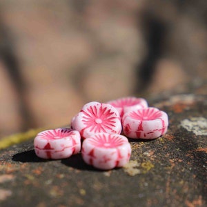 Può includere: Cinque bottoni di caramelle rosa e bianchi con un motivo floreale su una superficie ruvida e marrone.