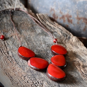 May include: A red seed necklace featuring five large, oval-shaped beads. The necklace is crafted from natural materials and has a rustic, earthy feel.