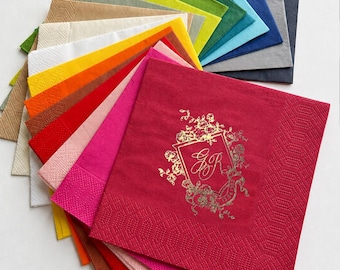 Può includere: Un ventaglio di tovaglioli di carta quadrati in un'ampia gamma di colori tra cui rosso, rosa, arancione, giallo, bianco, beige, verde, blu e grigio. Il tovagliolo rosso in cima presenta uno stemma dorato con le lettere GR e dettagli floreali.