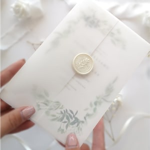 Puede incluir: Una invitaci&oacute;n de boda blanca con un sello de cera con un dise&ntilde;o de hoja. La invitaci&oacute;n tiene un dise&ntilde;o de acuarela de hojas y ramas verdes.