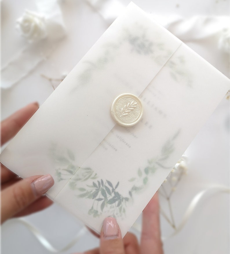 Puede incluir: Una invitaci&oacute;n de boda blanca con un sello de cera con un dise&ntilde;o de hoja. La invitaci&oacute;n tiene un dise&ntilde;o de acuarela de hojas y ramas verdes.