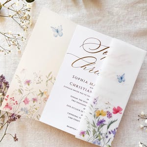Puede incluir: Una invitación de boda con motivos florales y mariposas. La invitación blanca presenta un borde floral en rosa, morado y amarillo. El texto incluye los nombres "Sophia y Christian" y los detalles del evento.