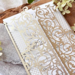 May include: Elegant gold laser-cut wedding invitation with intricate floral and lattice designs. The invitation features the names "Michael" and "Rachel" and event details. The design includes decorative borders and a classic, formal style.