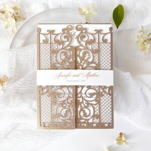 May include: A laser-cut wedding invitation in a gate design. The invitation is a light brown color with intricate scrollwork and a lattice pattern. The names "Jennifer and Matthew" and the date "November 1, 2025" are printed on a white band.