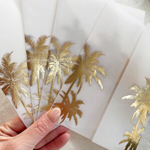 Peut inclure: Plusieurs enveloppes blanches orn&eacute;es de motifs de palmiers dor&eacute;s. Les enveloppes sont tenues, r&eacute;v&eacute;lant les d&eacute;tails dor&eacute;s. Chaque enveloppe pr&eacute;sente le m&ecirc;me motif, cr&eacute;ant un th&egrave;me tropical coh&eacute;rent.