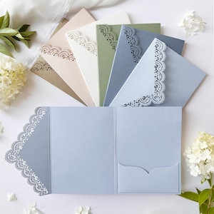 Puede incluir: Una colección de tarjeteros plegables en varios colores, incluyendo azul claro, verde salvia, crema y beige. Cada tarjetero presenta un patrón de encaje cortado con láser a lo largo de los bordes y un pequeño bolsillo interior para insertar tarjetas.