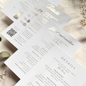 Puede incluir: Una pila de tarjetas de detalles de boda blancas con texto impreso en negro y detalles en l&aacute;mina de oro. Las tarjetas incluyen secciones para transporte, recepci&oacute;n y c&oacute;digo de vestimenta, junto con un c&oacute;digo QR y una URL de sitio web.