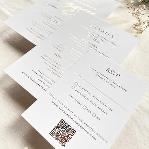 Puede incluir: Un conjunto de invitaciones de boda blancas con letras en l&aacute;mina dorada y un c&oacute;digo QR. El set incluye una tarjeta de invitaci&oacute;n principal con las iniciales E/J, una tarjeta de detalles y una tarjeta RSVP con casillas de verificaci&oacute;n.