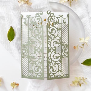 May include: A sage green laser-cut wedding invitation with an ornate gate design. The invitation features the names of the couple and the wedding date, October 15, 2029. The invitation is on a white background with floral accents.