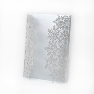 May include: A silver card with a snowflake design on the right side and a snowflake border on the left side.