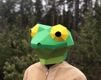 May include: A green and yellow paper mache frog mask. The mask is made of folded paper and has a three-dimensional design.