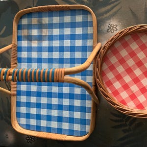 May include: A rectangular wicker serving tray with a blue and white checkered pattern, and a round wicker basket with a red and white checkered pattern. The tray has a curved handle with blue accents.