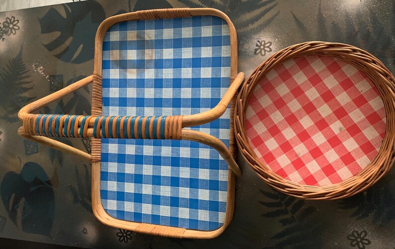 May include: A rectangular wicker serving tray with a blue and white checkered pattern, and a round wicker basket with a red and white checkered pattern. The tray has a curved handle with blue accents.