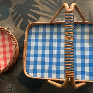 May include: Two vintage picnic baskets. One is round with a red and white checkered pattern, and the other is rectangular with a blue and white checkered pattern. Both have woven wicker frames.