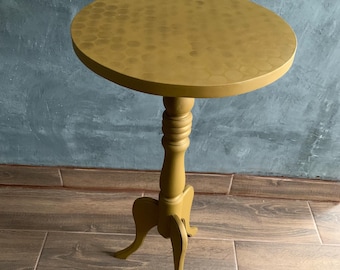 May include: Mustard yellow accent table with a round top featuring a honeycomb pattern. The table has a pedestal base and three curved legs. The table is approximately 24 inches tall and 18 inches in diameter.