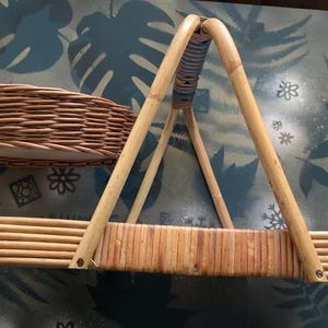 May include: Two woven wicker baskets. One is a shallow, oval shape. The other is a rectangular basket with a handle. The handle is made of bamboo and is attached to the basket with metal fasteners. The baskets are brown.