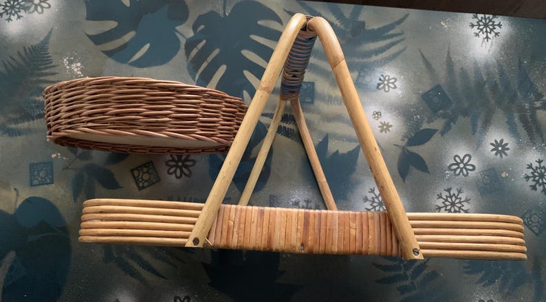May include: Two woven wicker baskets. One is a shallow, oval shape. The other is a rectangular basket with a handle. The handle is made of bamboo and is attached to the basket with metal fasteners. The baskets are brown.
