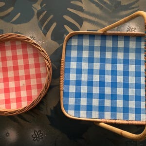 May include: Two wicker serving trays. One is round with a red and white checkered pattern. The other is rectangular with a blue and white checkered pattern and a handle. The handle is wrapped with blue and brown material.