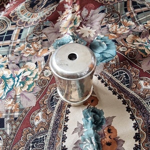 K&ouml;nnte beinhalten: Ein silberfarbener, zylindrischer Beh&auml;lter mit einem Loch in der Mitte des Deckels. Der Beh&auml;lter ist reflektierend und liegt auf einem gemusterten Stoff mit Blumen- und Paisley-Designs in Braun-, Blau- und Cremet&ouml;nen.