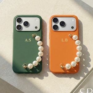 May include: Two phone cases, one green and one orange, are displayed. Each case has a pearl bracelet attached and personalized initials. The green case has the initials "A.S" and the orange case has the initials "L.B".