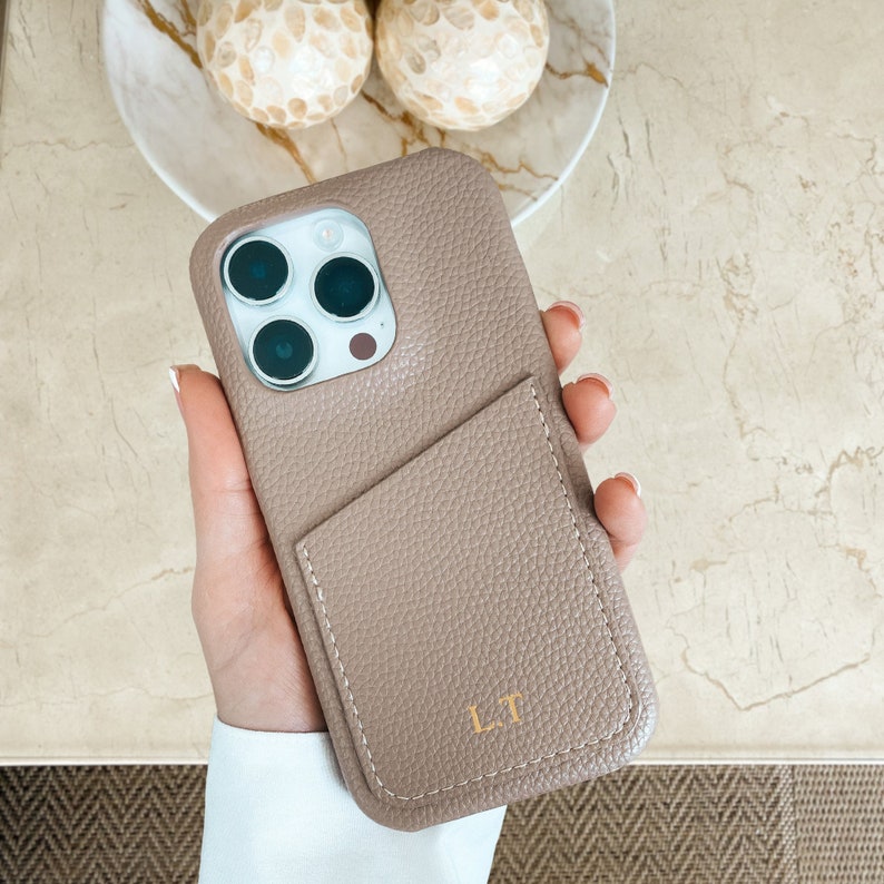 May include: A light brown leather phone case with a pocket and the initials "LT" embossed on the front.