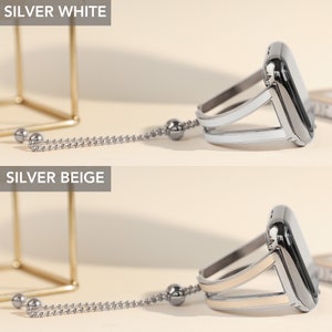 May include: Two silver Apple Watch bands with a chain and a charm. The band on the top is white and the band on the bottom is beige.