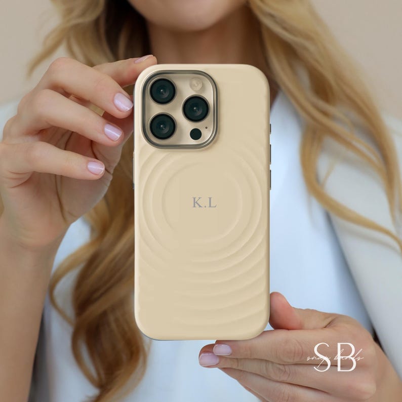Puede incluir: Funda de tel&eacute;fono beige claro con dise&ntilde;o en espiral y las iniciales "K.L.". La funda tiene un m&oacute;dulo de c&aacute;mara con tres lentes. La funda es de color beige claro.