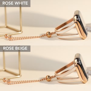 May include: Two Apple Watch bands with a rose gold finish and a white or beige strap. The bands have a chain attached to the top of the band.