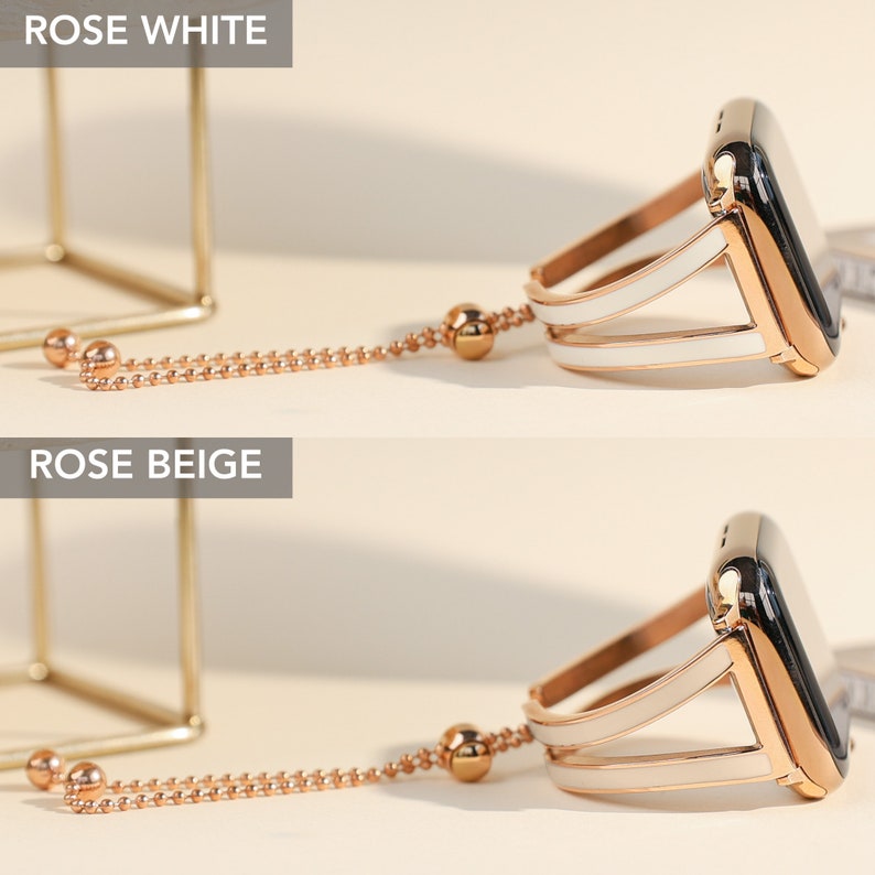May include: Two Apple Watch bands with a rose gold finish and a white or beige strap. The bands have a chain attached to the top of the band.