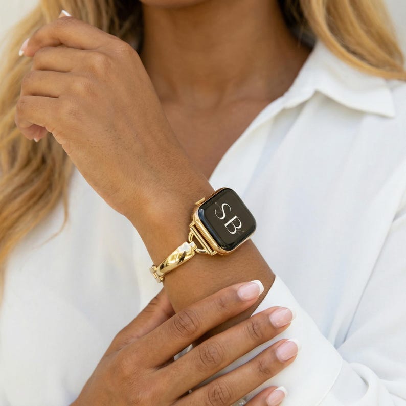 May include: Gold-toned watch band with a black watch face. The watch face displays the initials "SB" in white. The band has a textured, braided design. The watch is worn on a wrist.
