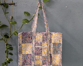 May include: A patchwork tote bag with floral and geometric patterns in shades of pink, yellow, and blue. The bag has a single compartment and two long straps.
