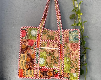 May include: A patchwork tote bag with red and white striped trim. The bag is made of different fabrics with floral and geometric patterns in shades of green, brown, orange, and pink. The bag is hanging on a hook.