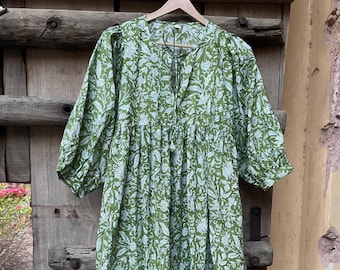 May include: A green maxi dress with a white floral print. The dress has a V-neckline and a tie at the neckline. The sleeves are puffed and end at the elbow.
