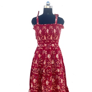 May include: A burgundy sundress with a floral pattern. The dress features a smocked bodice, tie straps, and a tiered skirt. The floral design includes white and peach-colored flowers and leaves.