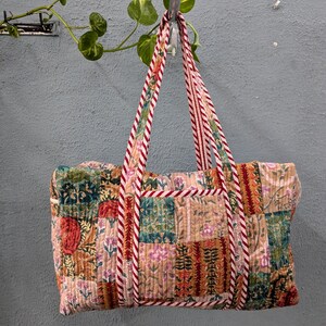 May include: A patchwork style tote bag with red and white striped straps. The bag is made of quilted fabric with a variety of floral patterns in shades of pink, green, brown, and orange.