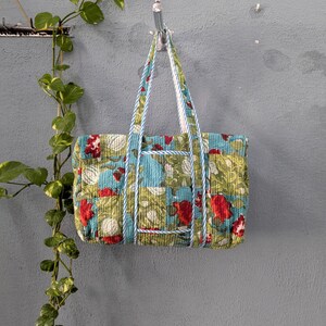 May include: A blue and green floral print tote bag with white and blue trim. The bag has two straps and is hanging on a hook.