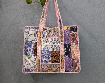 May include: A patchwork tote bag with a pink and white striped trim. The bag is made of different fabrics with floral and geometric patterns in shades of blue, purple, brown, and white.