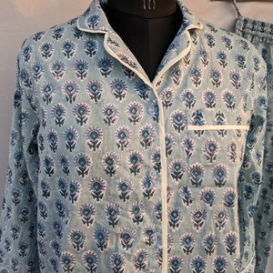 May include: A light blue pajama top with a white trim and a floral print. The top has a button-up front and long sleeves.